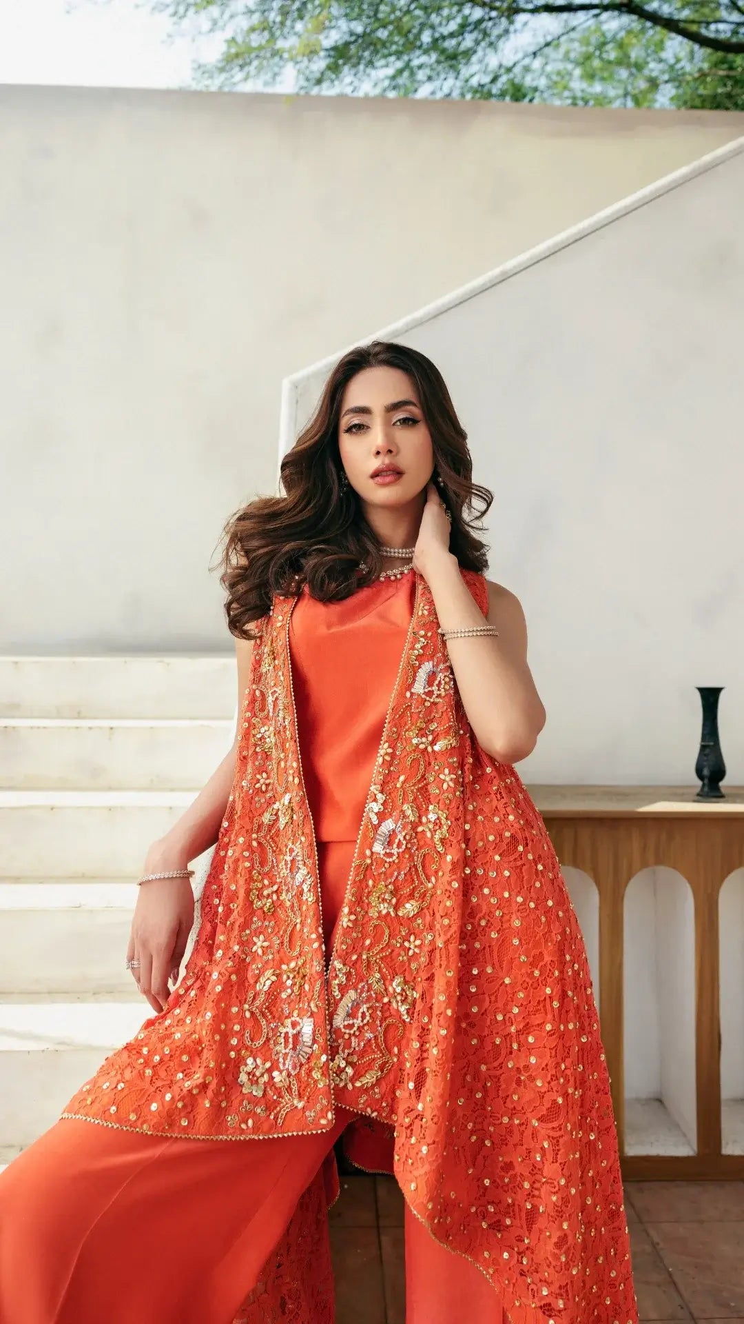 Woman wearing an orange outfit with a matching shawl indoors.
