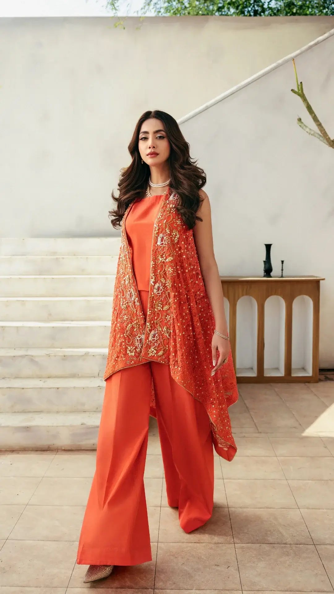 Woman in an orange traditional outfit standing in a well-lit room with a staircase.