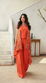 Woman in an orange outfit with a matching vest standing in a modern interior setting.