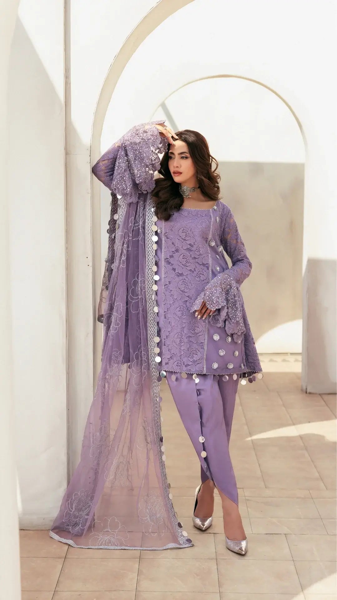 Woman in a purple embroidered outfit with a sheer dupatta in an indoor setting