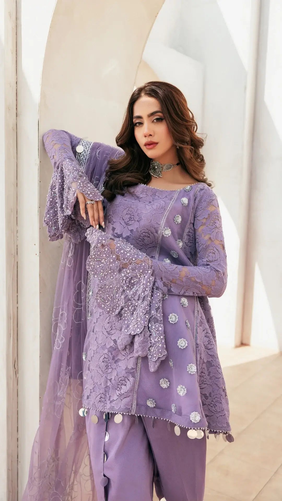 Woman wearing a purple embroidered outfit with a sheer dupatta in a bright setting
