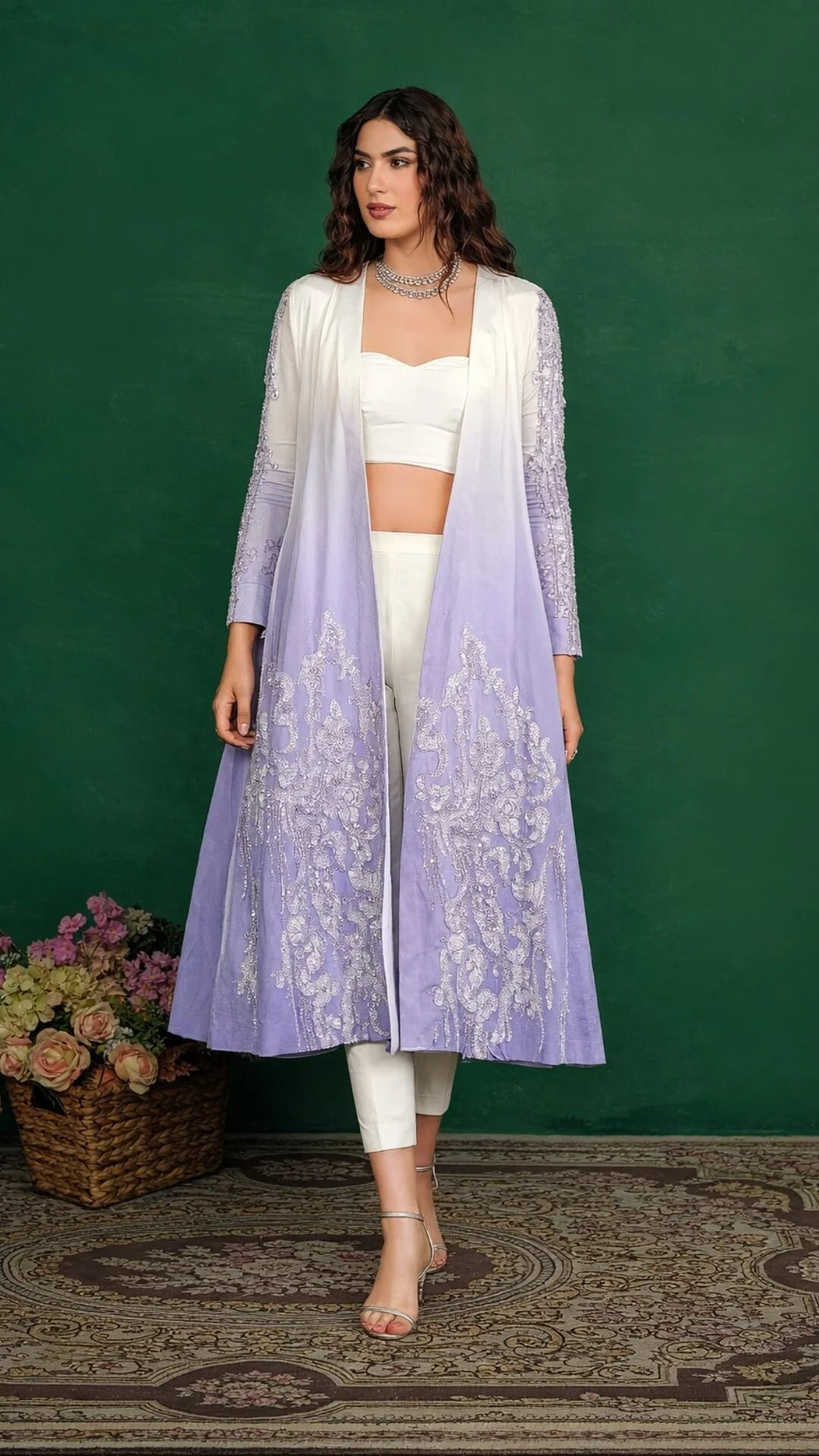 Woman wearing a long light purple embroidered jacket over a white outfit against a green background