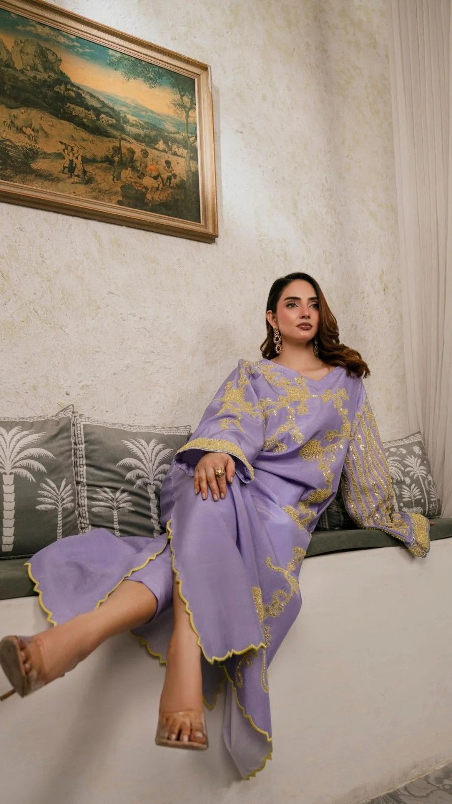 Woman in a purple traditional outfit sitting on a white ledge with a painting in the background.