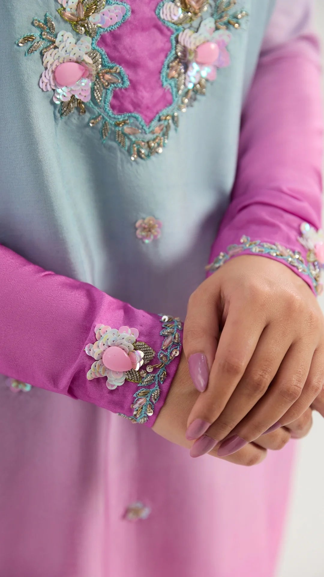 Close-up of a person wearing a pink outfit with floral embroidery on a plain background