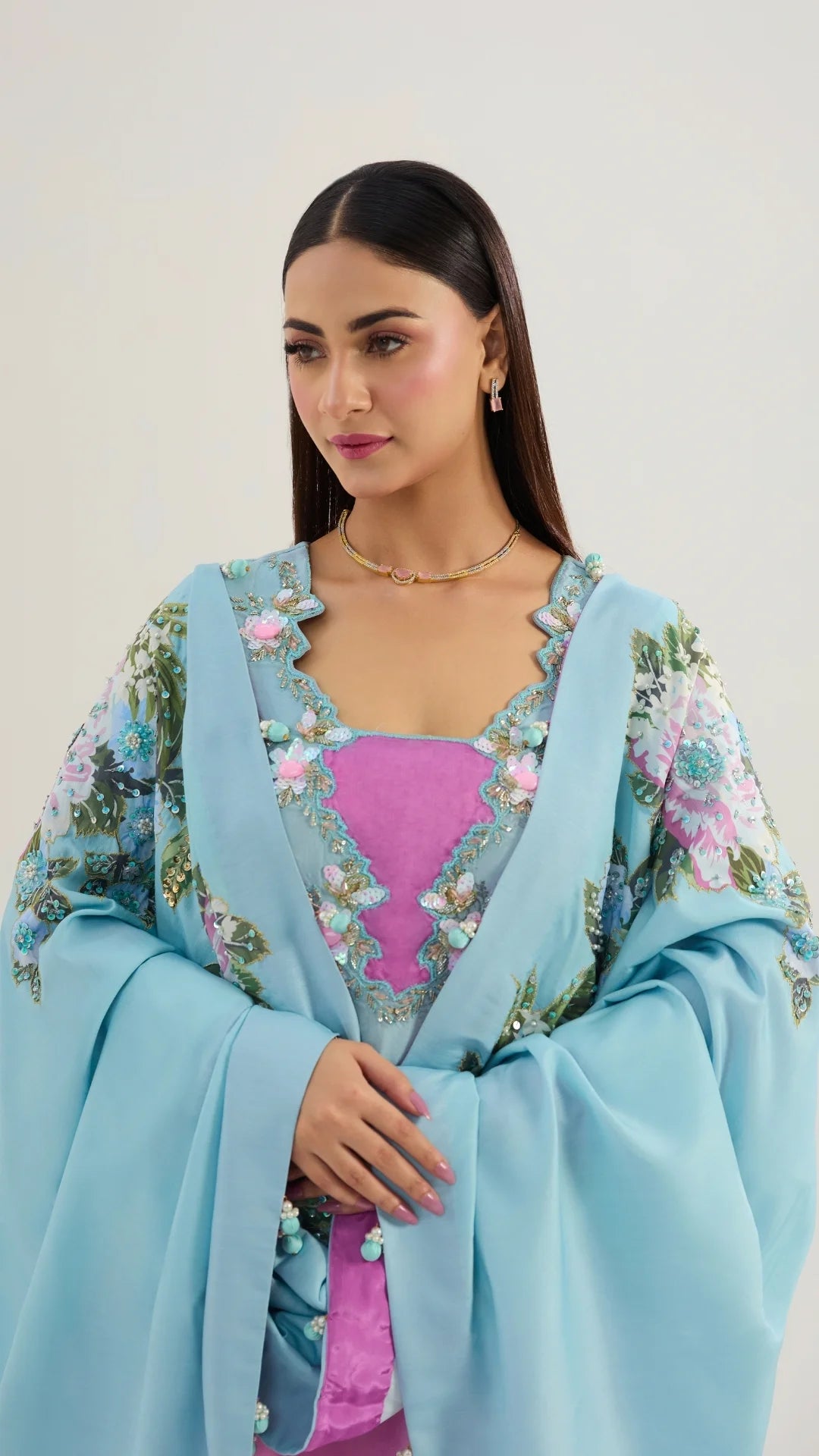 Woman wearing a light blue embroidered outfit with a pink top against a white background
