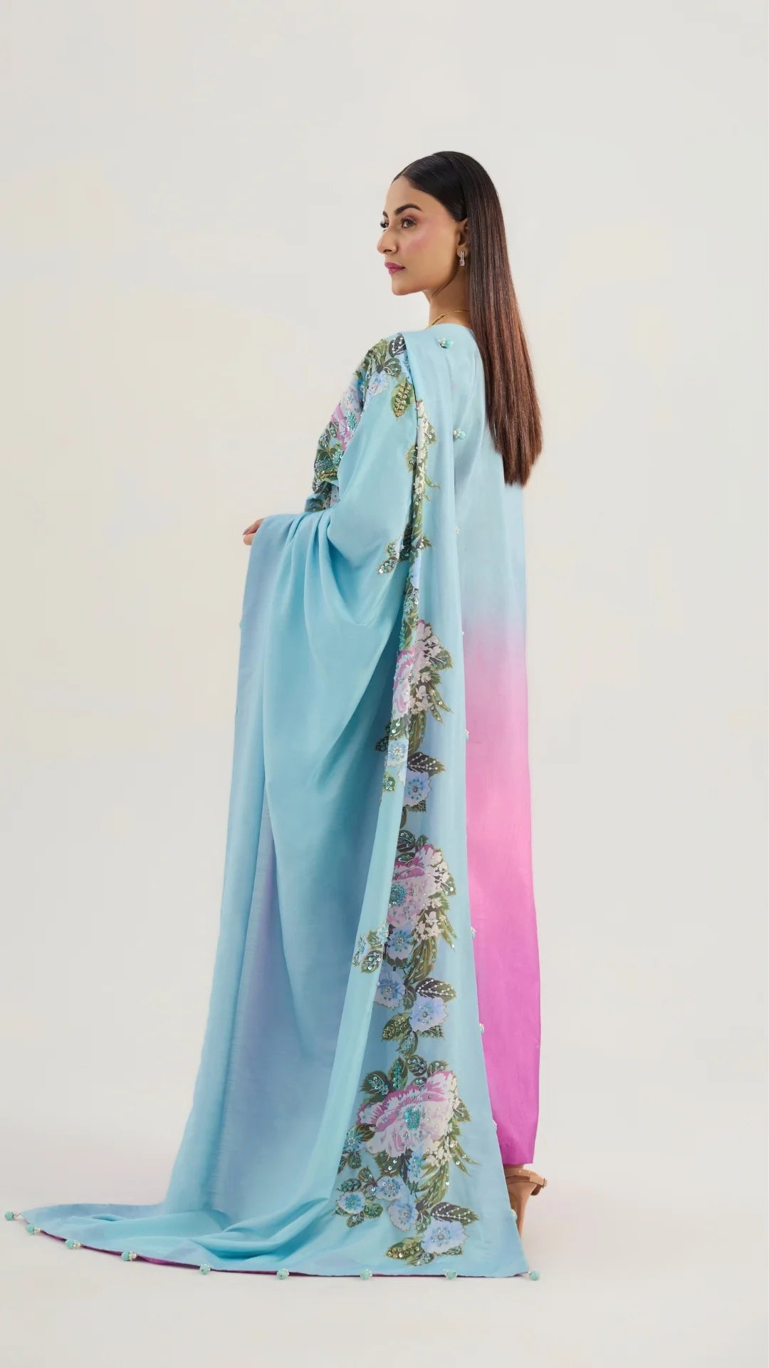 Woman wearing a long, light blue dress with floral embroidery on a plain background