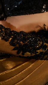 Close-up of a black sequined glove on a gold and black outfit.