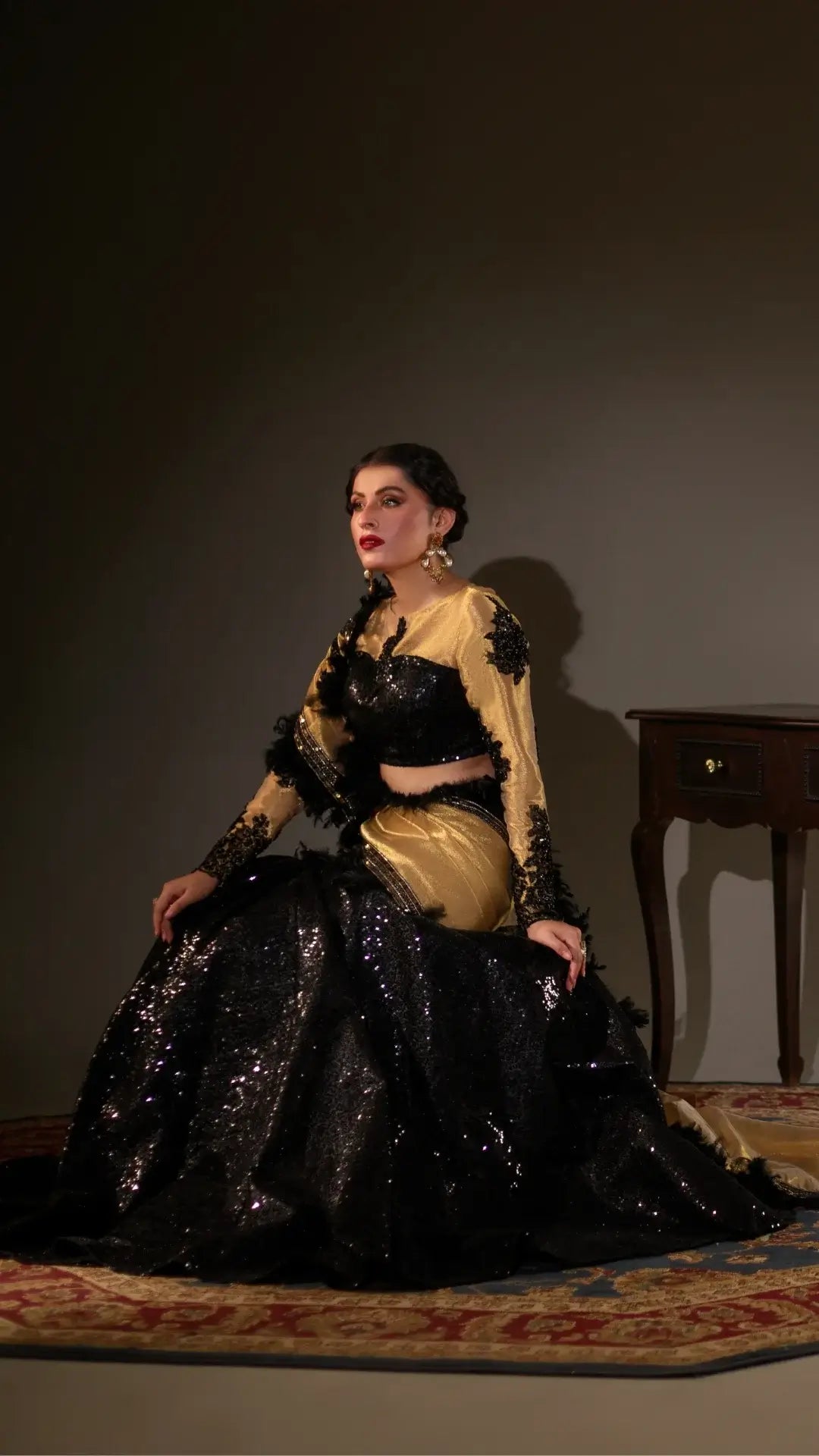 Woman in a black and gold traditional outfit sitting on a patterned rug.