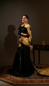Woman in a black and gold traditional outfit standing against a dark background