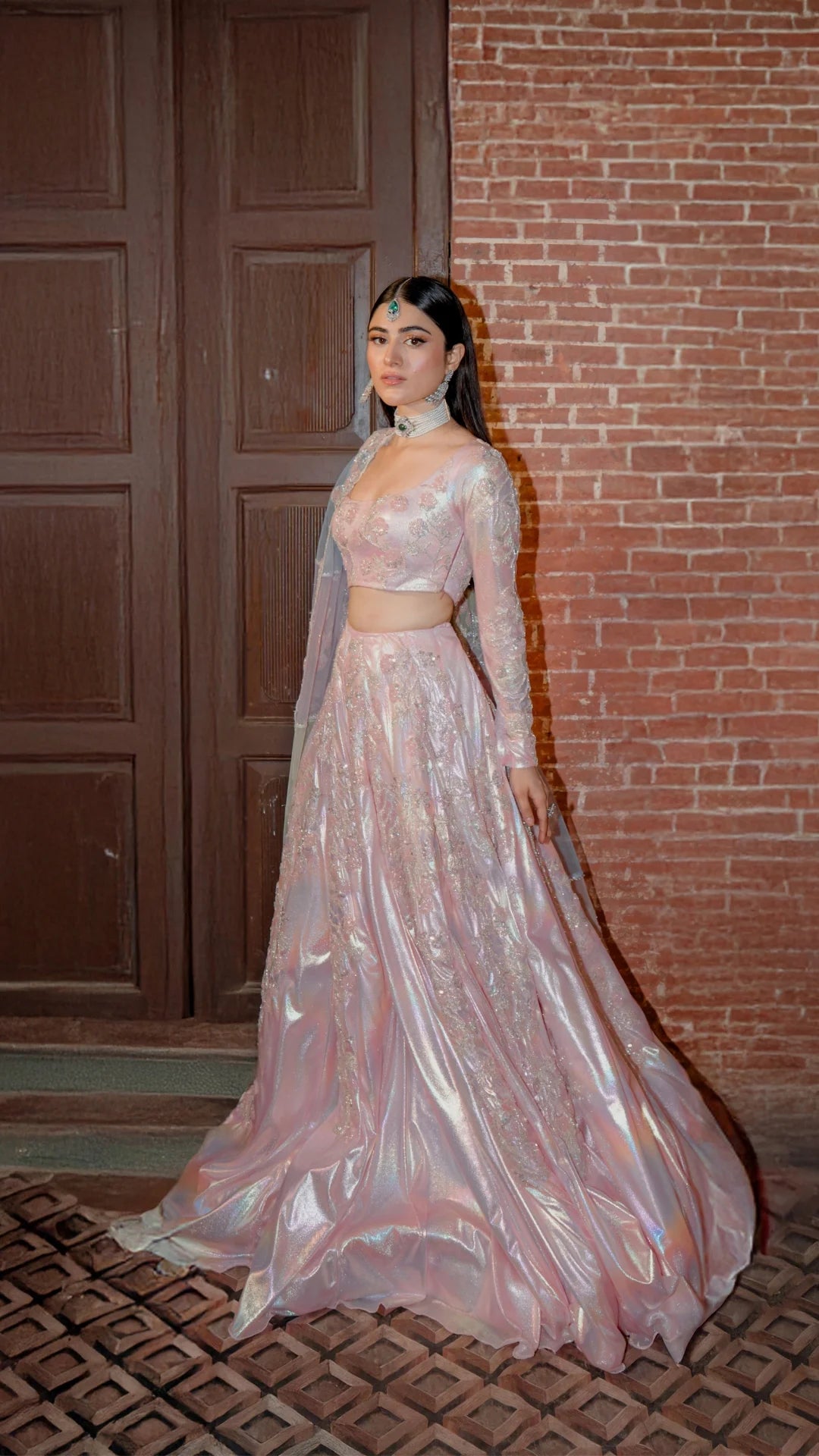 Woman in a pink traditional outfit standing against a brick wall.