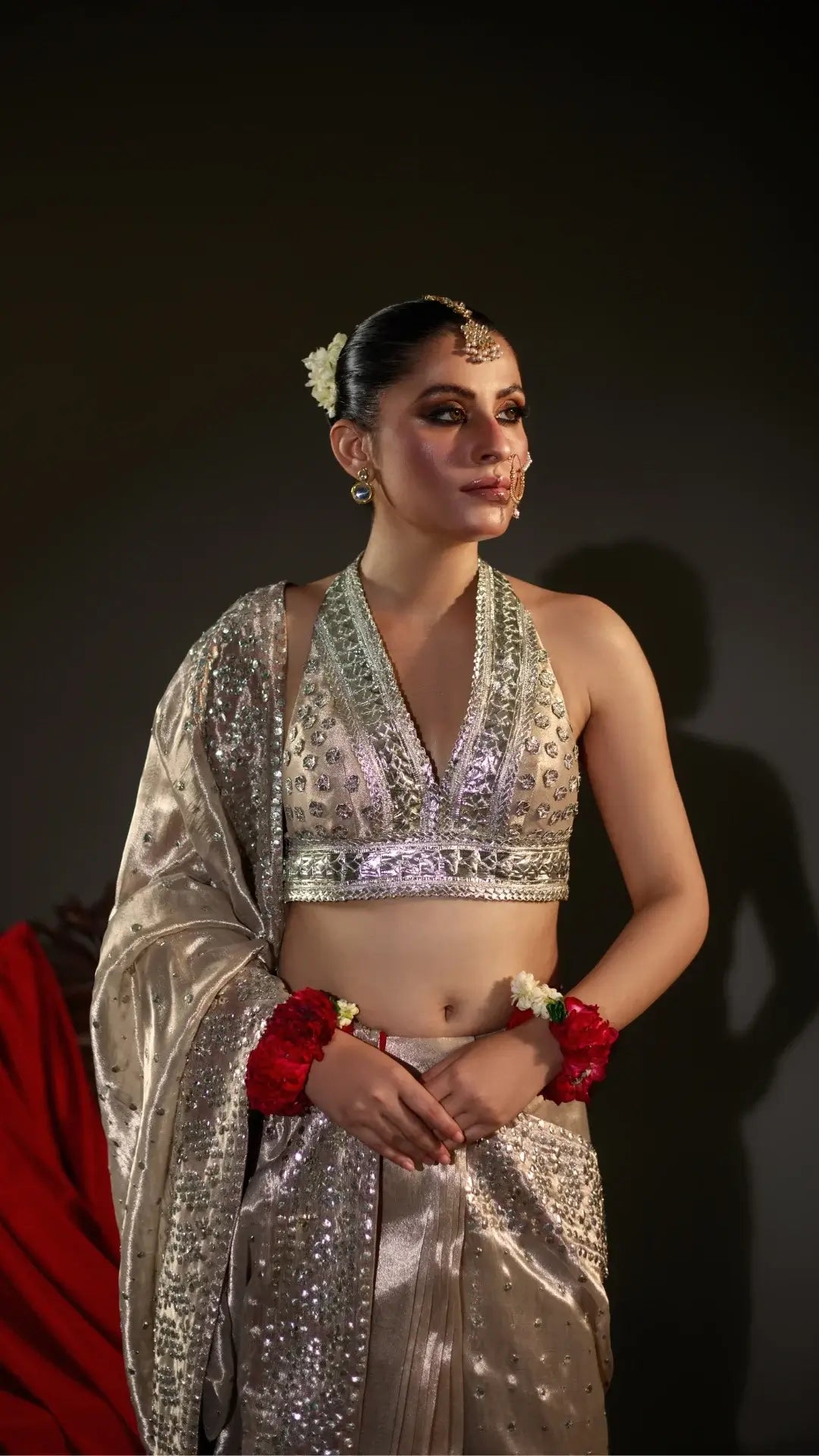 Woman in traditional silver and red outfit with jewelry against a dark background