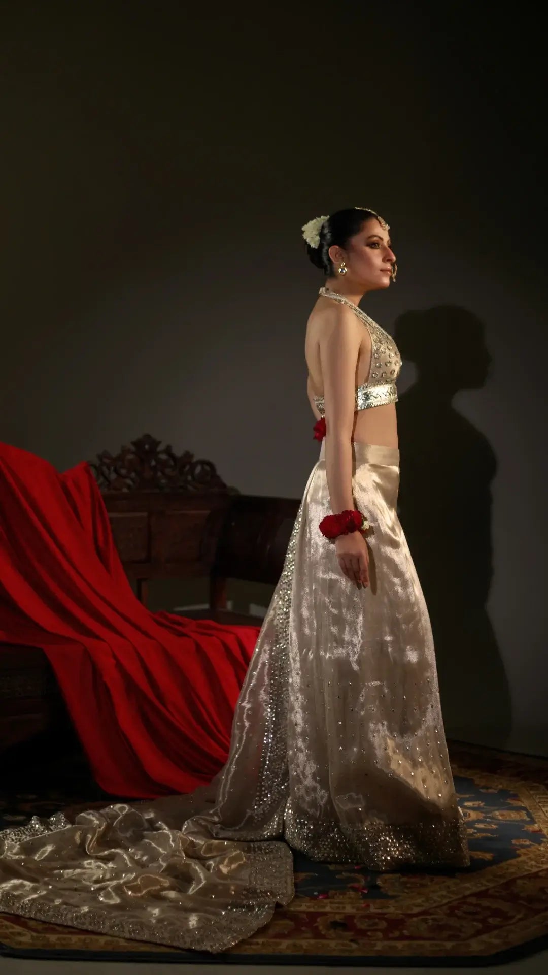 Woman in a sparkling silver outfit with red accents standing against a dark background