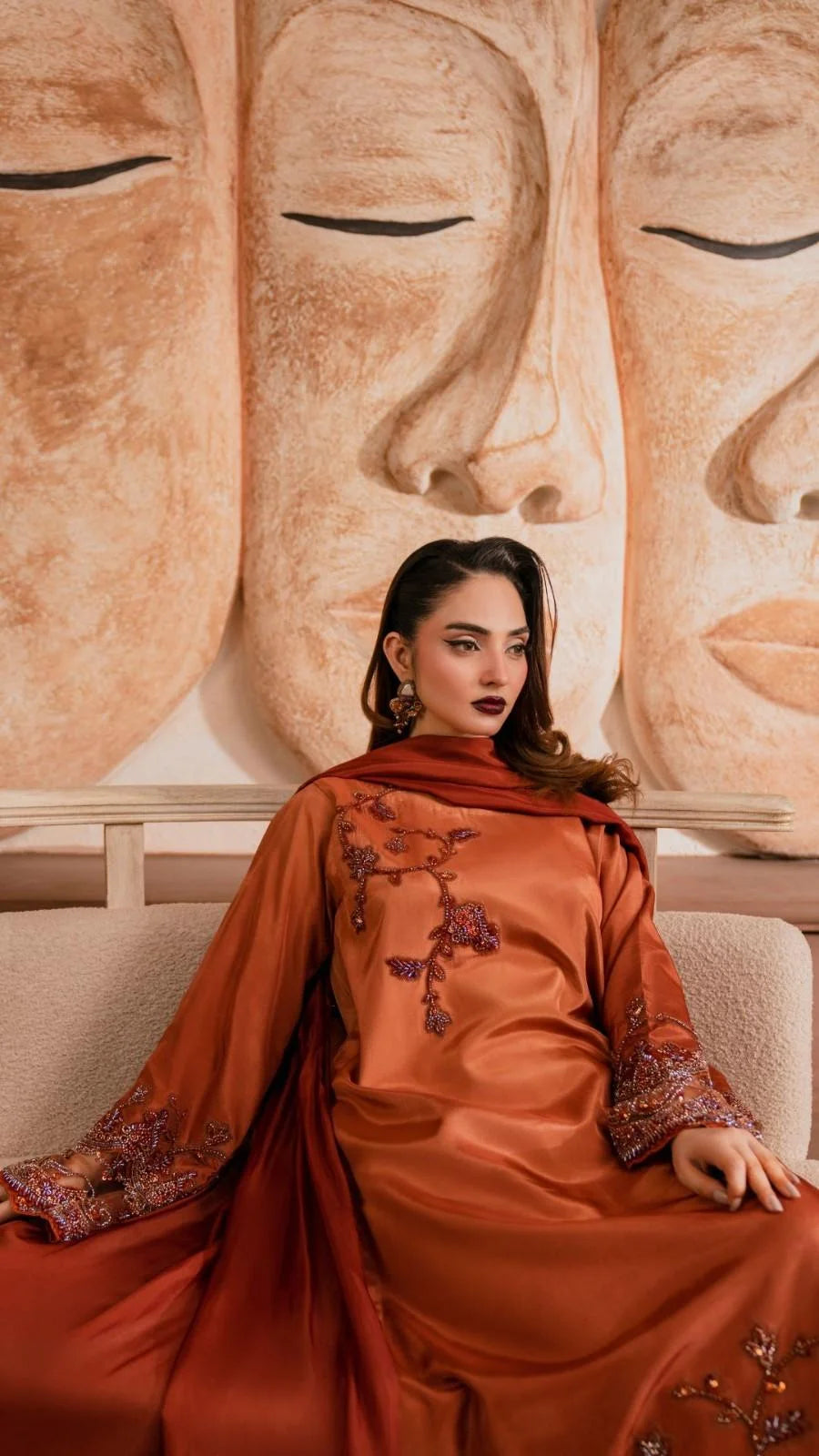 Woman in an orange traditional outfit sitting in front of a large Buddha statue.