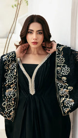 Woman wearing a black dress with gold embroidery against a white background