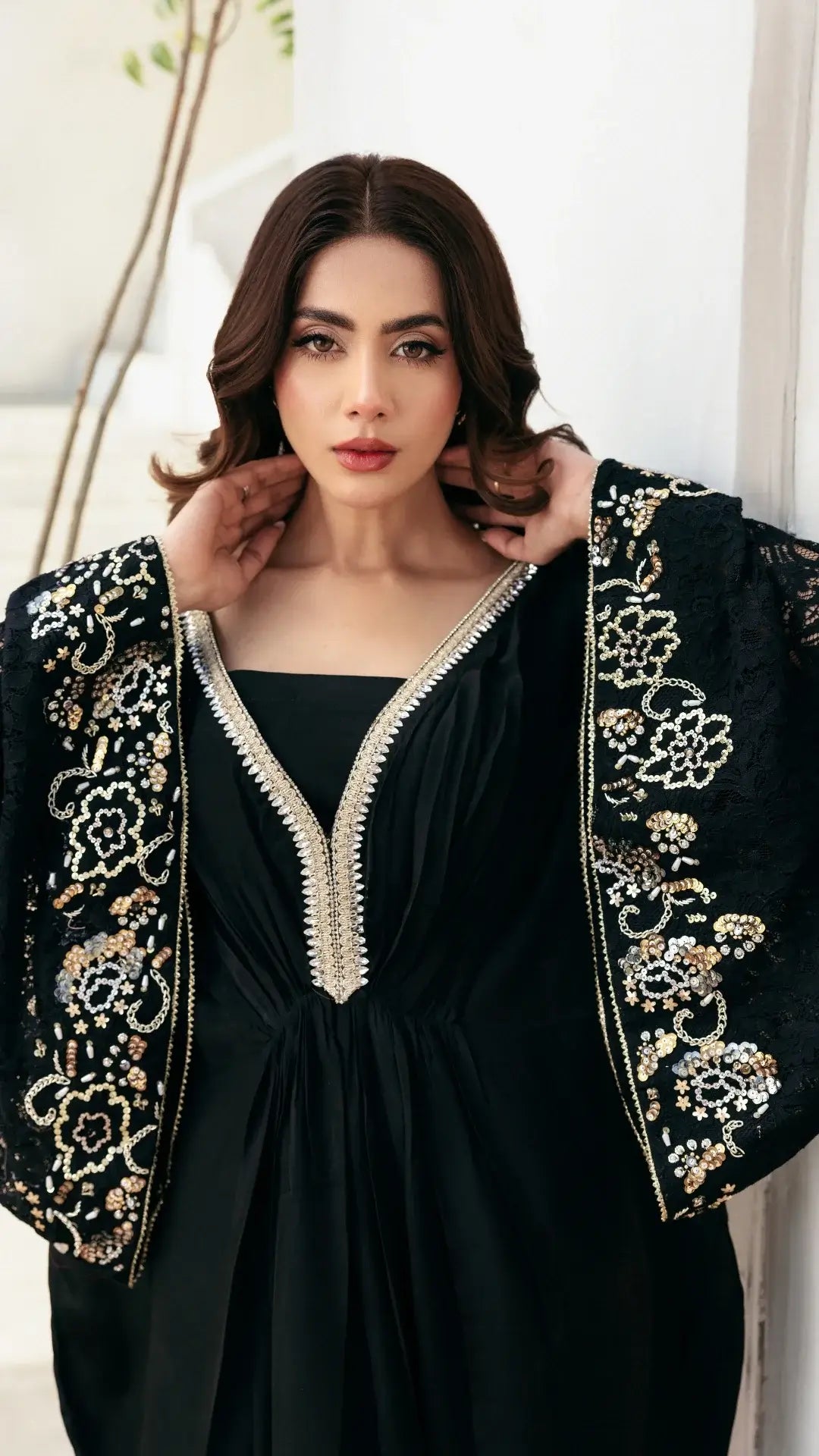 Woman wearing a black dress with gold embroidery against a white background