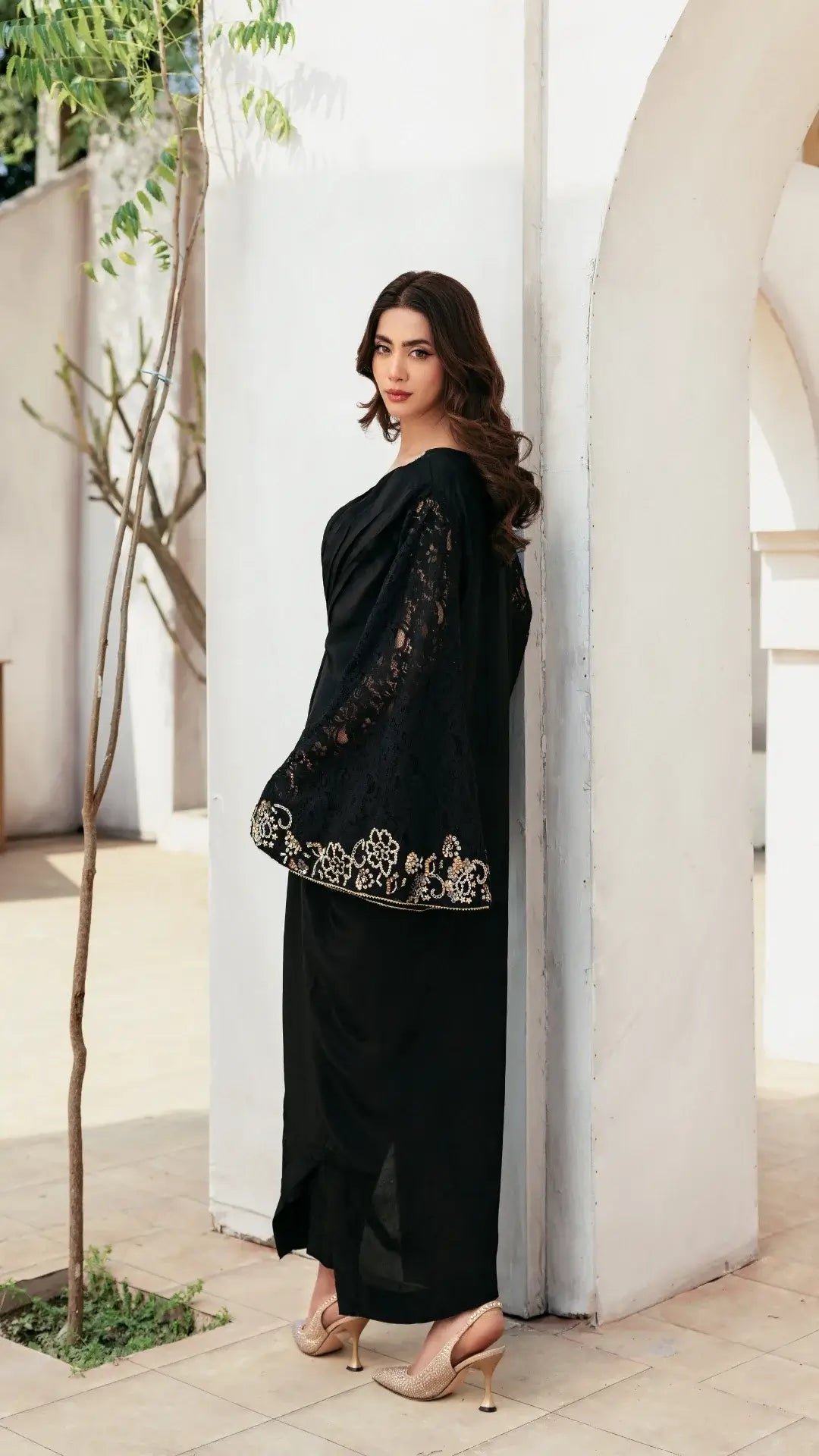 Woman in a black saree with floral embroidery standing in a bright, minimalistic indoor setting.