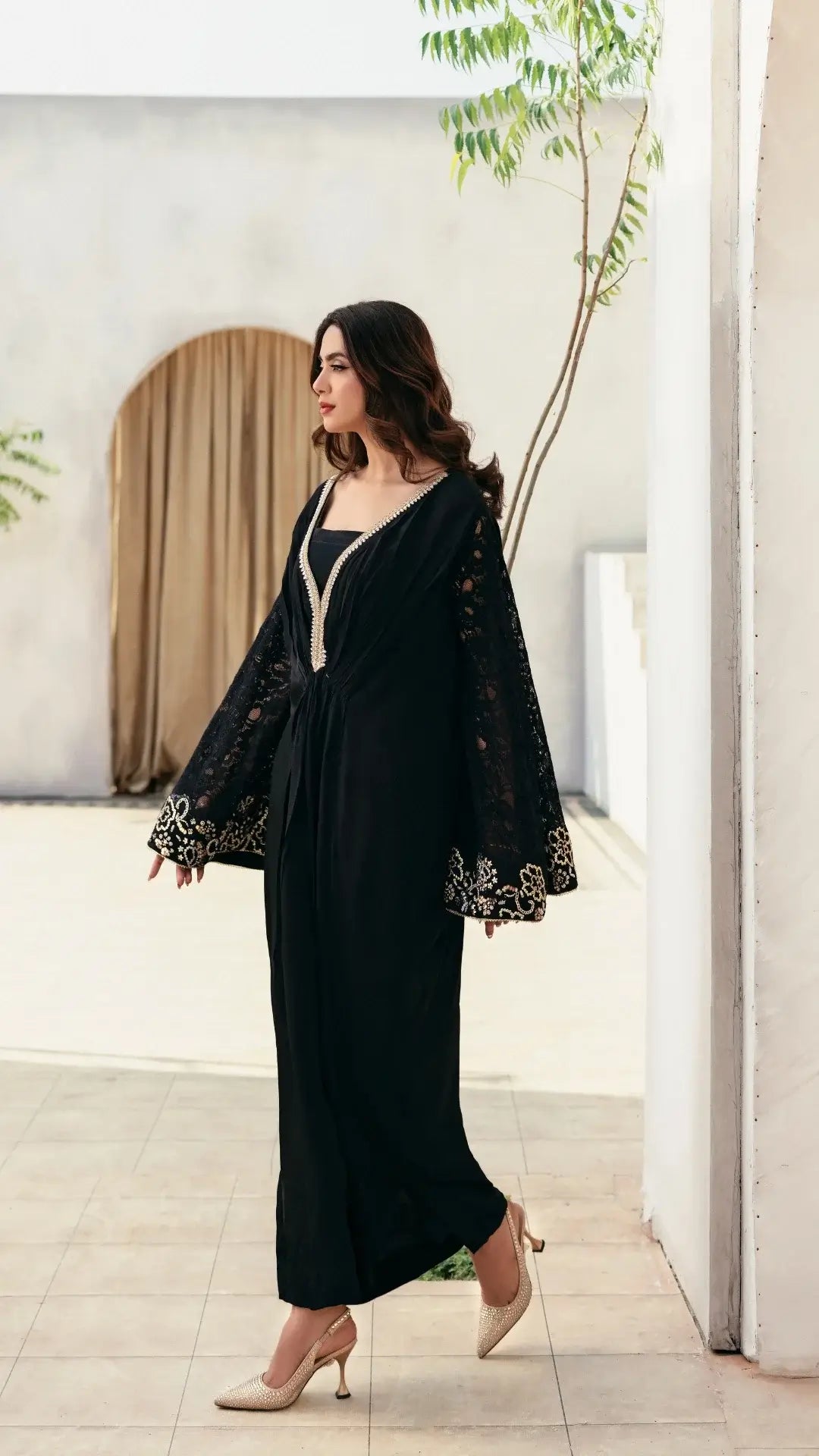 Woman wearing a black abaya with gold embroidery in an indoor setting.