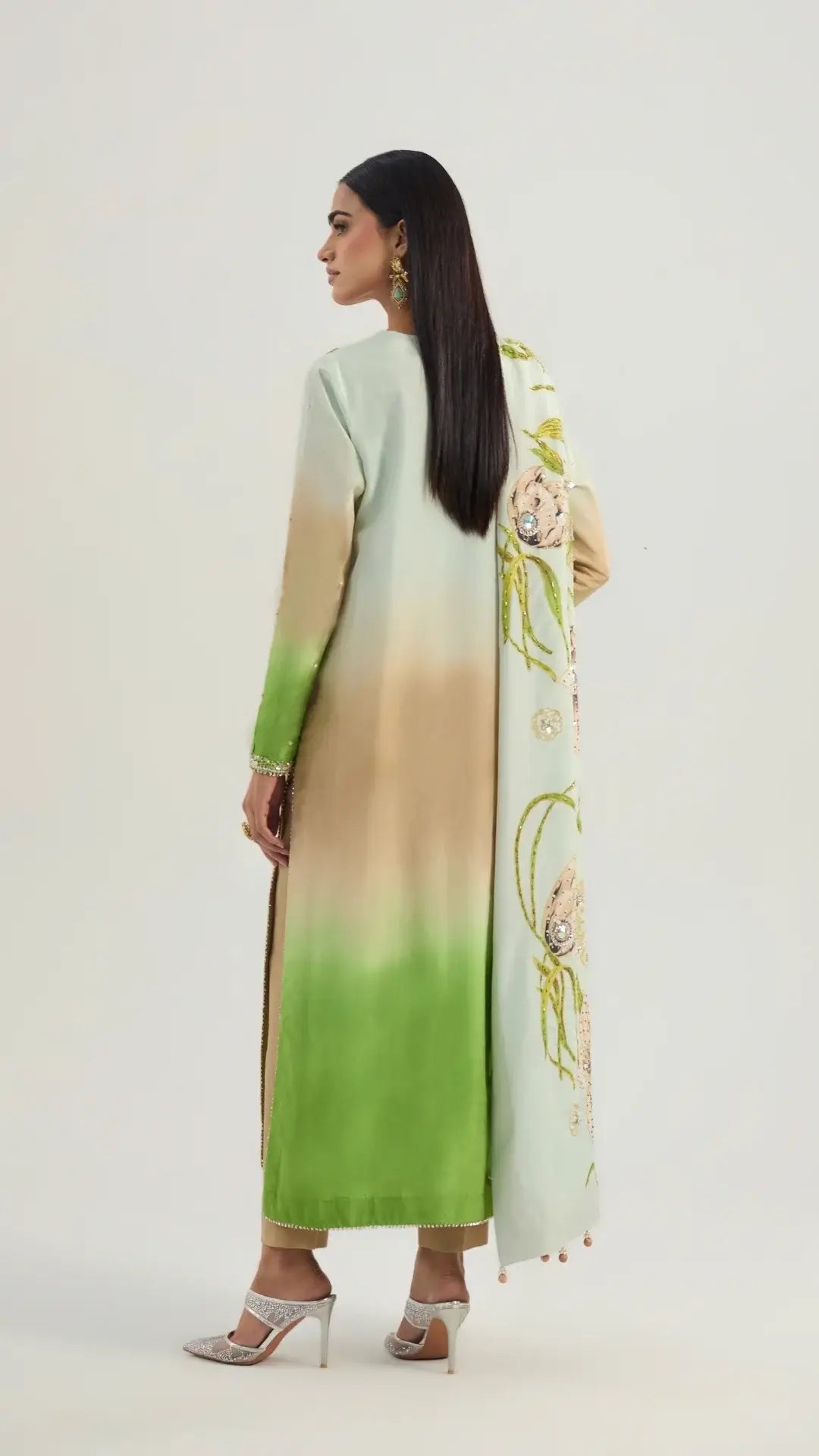 Woman wearing a long, gradient dress with a floral scarf on a white background