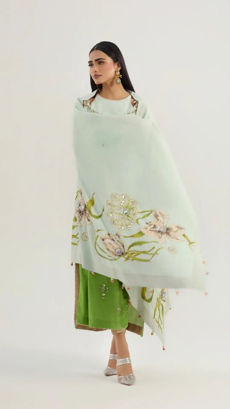 Woman wearing a light green floral-patterned shawl over a green outfit on a white background