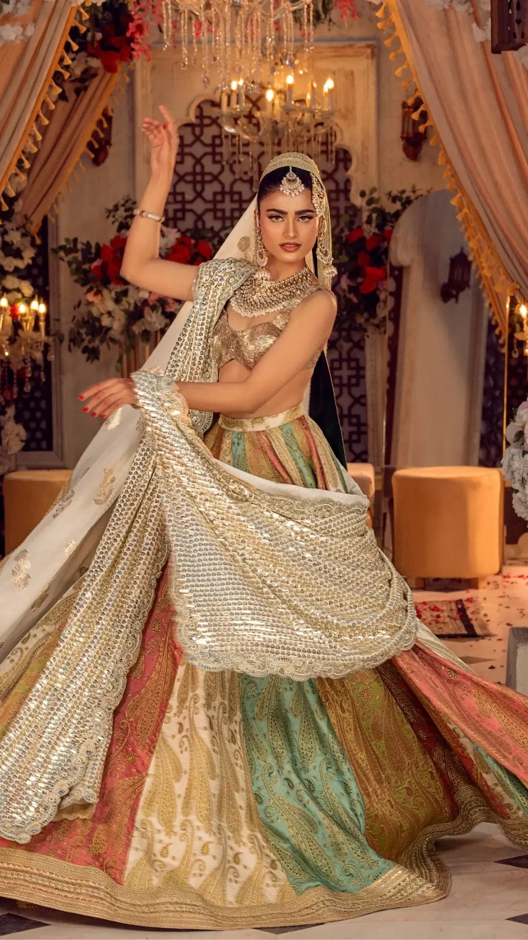 Woman in a traditional multicolored outfit with intricate designs, standing in an ornate decorated room.