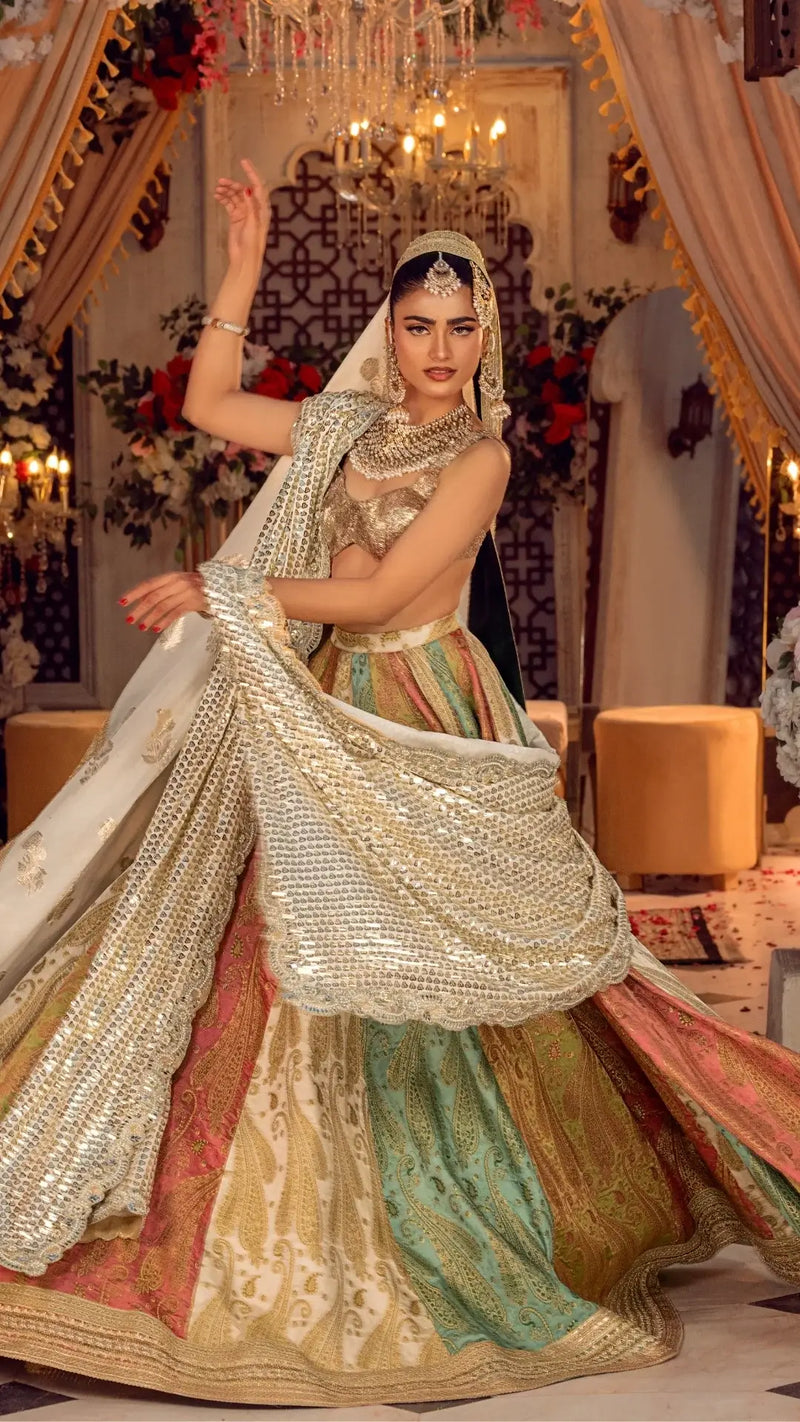 Woman in luxury Pakistani bridal dress with gold embellishments and colorful lehenga, posing indoors