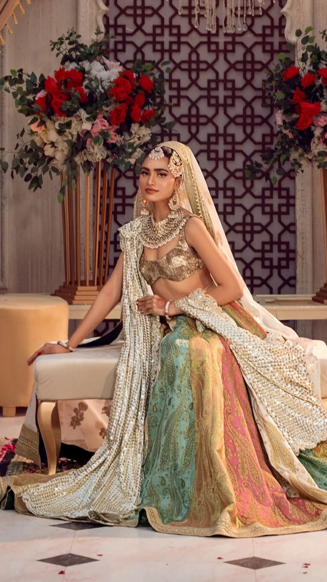 Woman in traditional attire sitting in an ornate room with floral decorations.