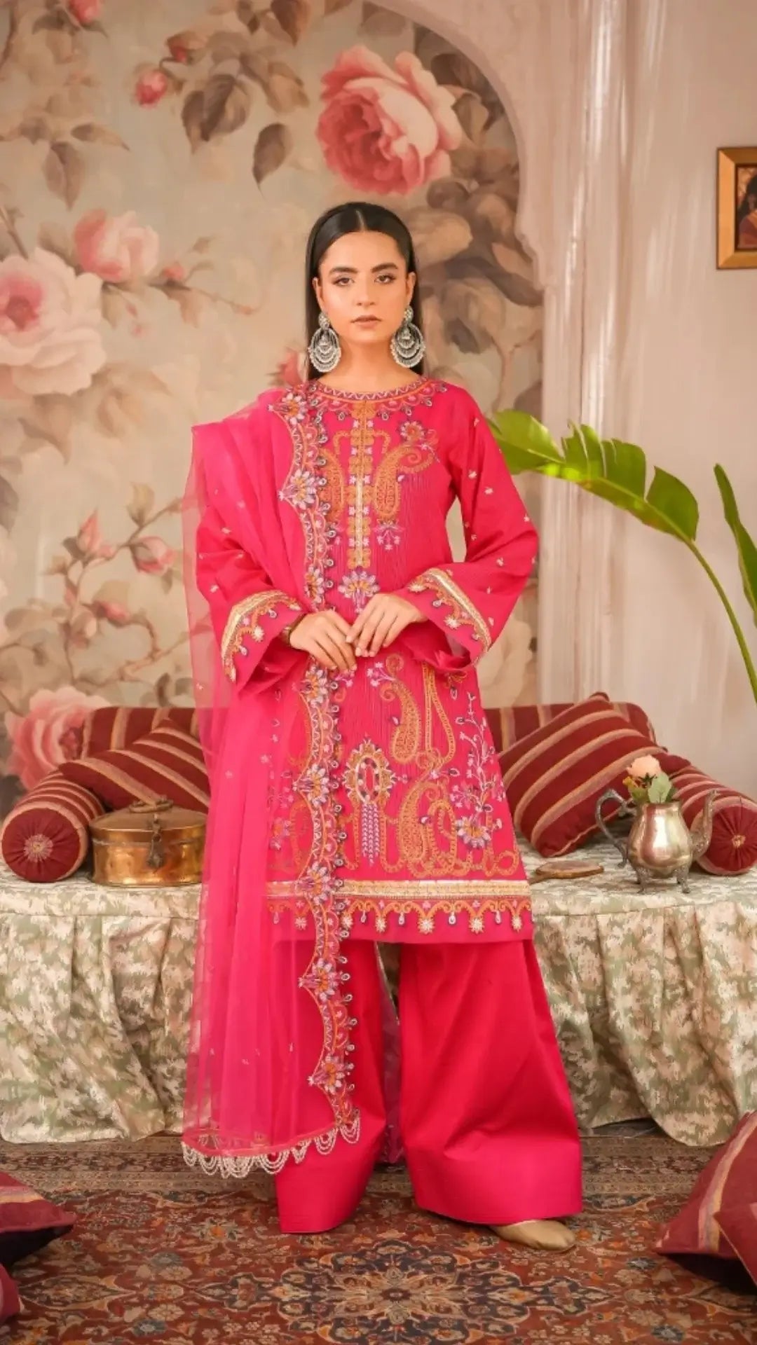 Woman in a bright pink embroidered traditional outfit standing in a decorated room.