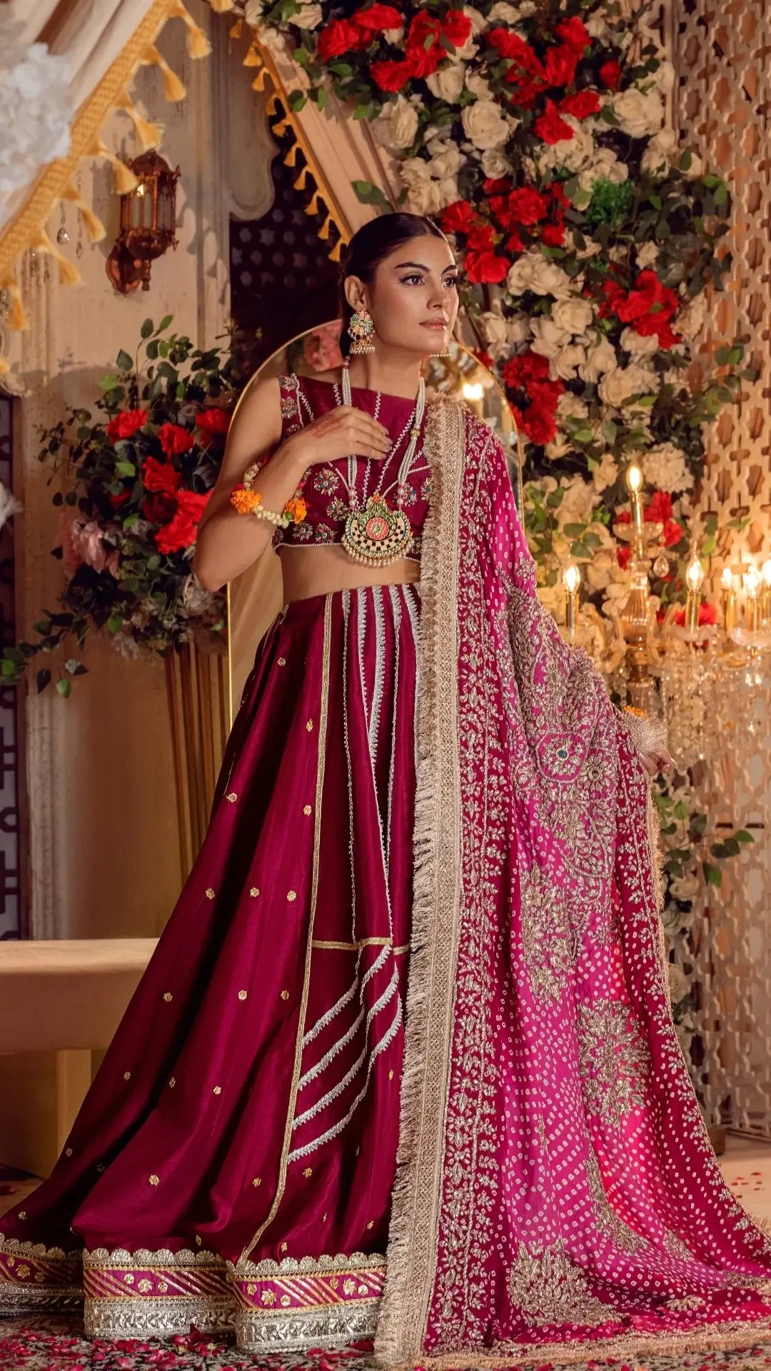 Woman in fuchsia bridal lehenga with gold embroidery and dupatta at a floral decorated venue