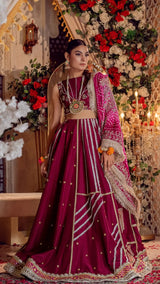Woman in fuchsia Pakistani formal dress with gold embroidery, floral dupatta, and jewelry, standing in elegant, flower-adorned setting.