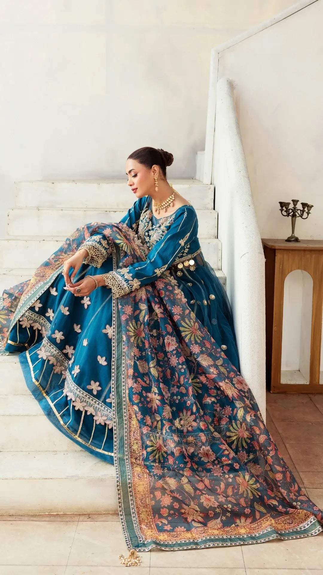 Woman in a blue and floral traditional outfit sitting on a staircase.