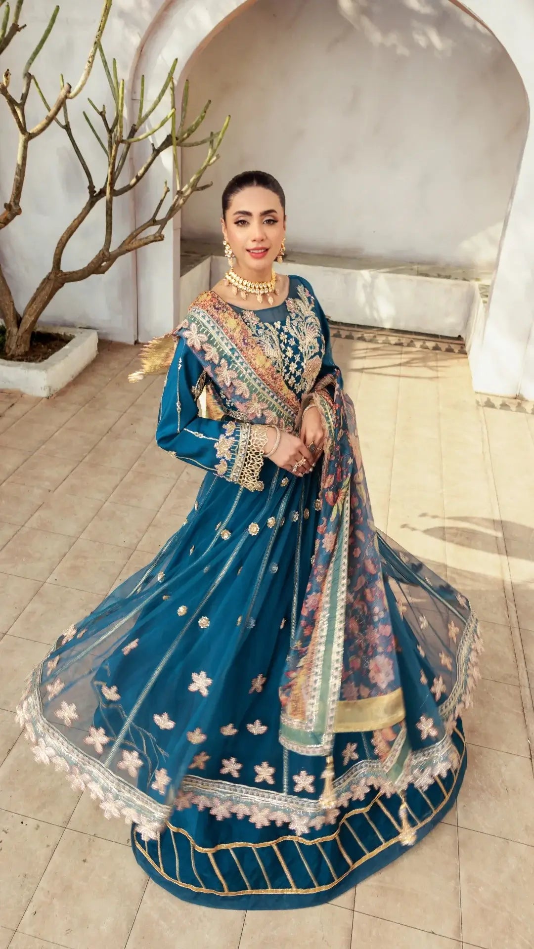 Woman in a traditional blue embroidered outfit standing indoors.