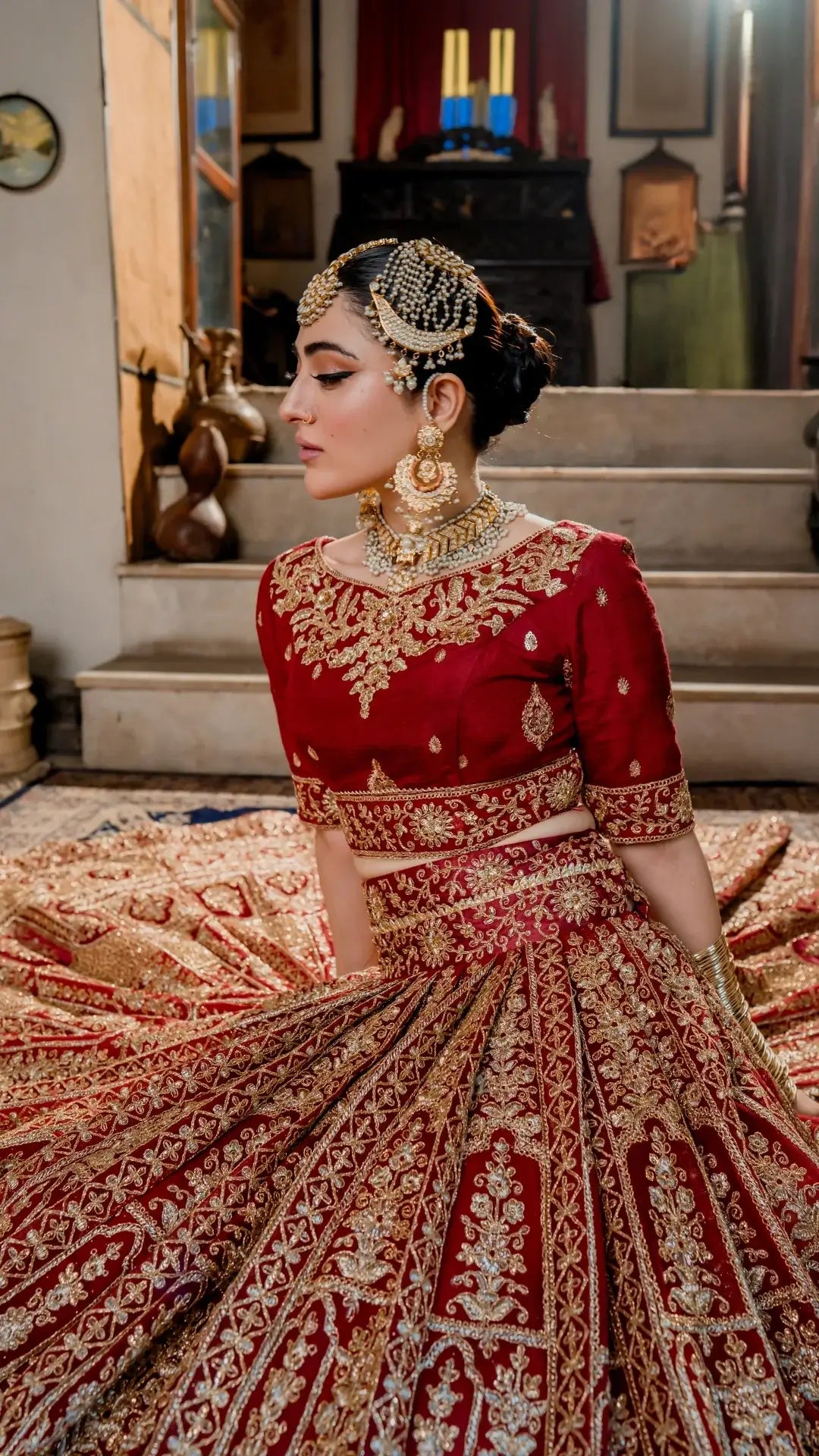 Woman in a red and gold traditional outfit with intricate designs, sitting on a patterned rug.