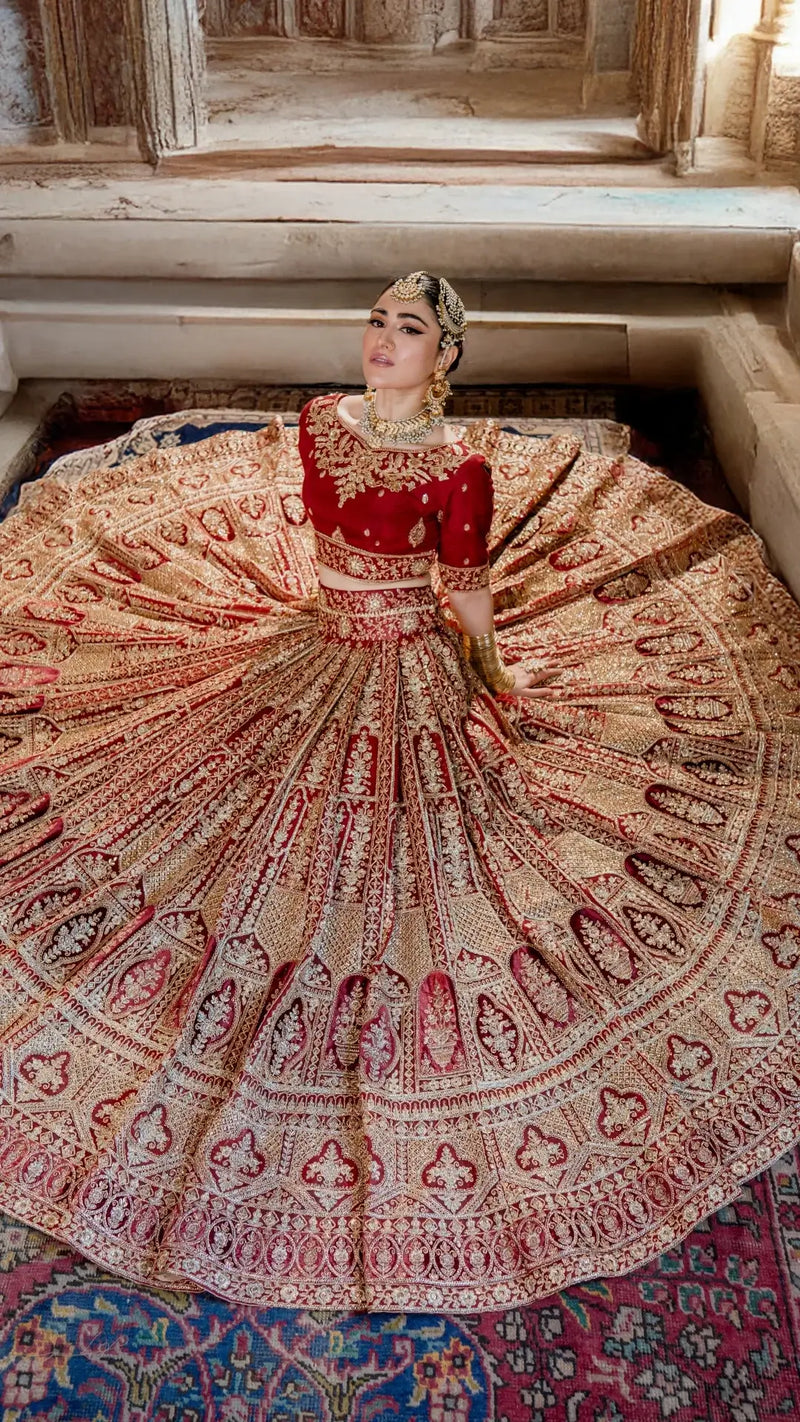 Woman in ornate red and gold embroidered bridal lehenga with jewelry, seated in heritage setting