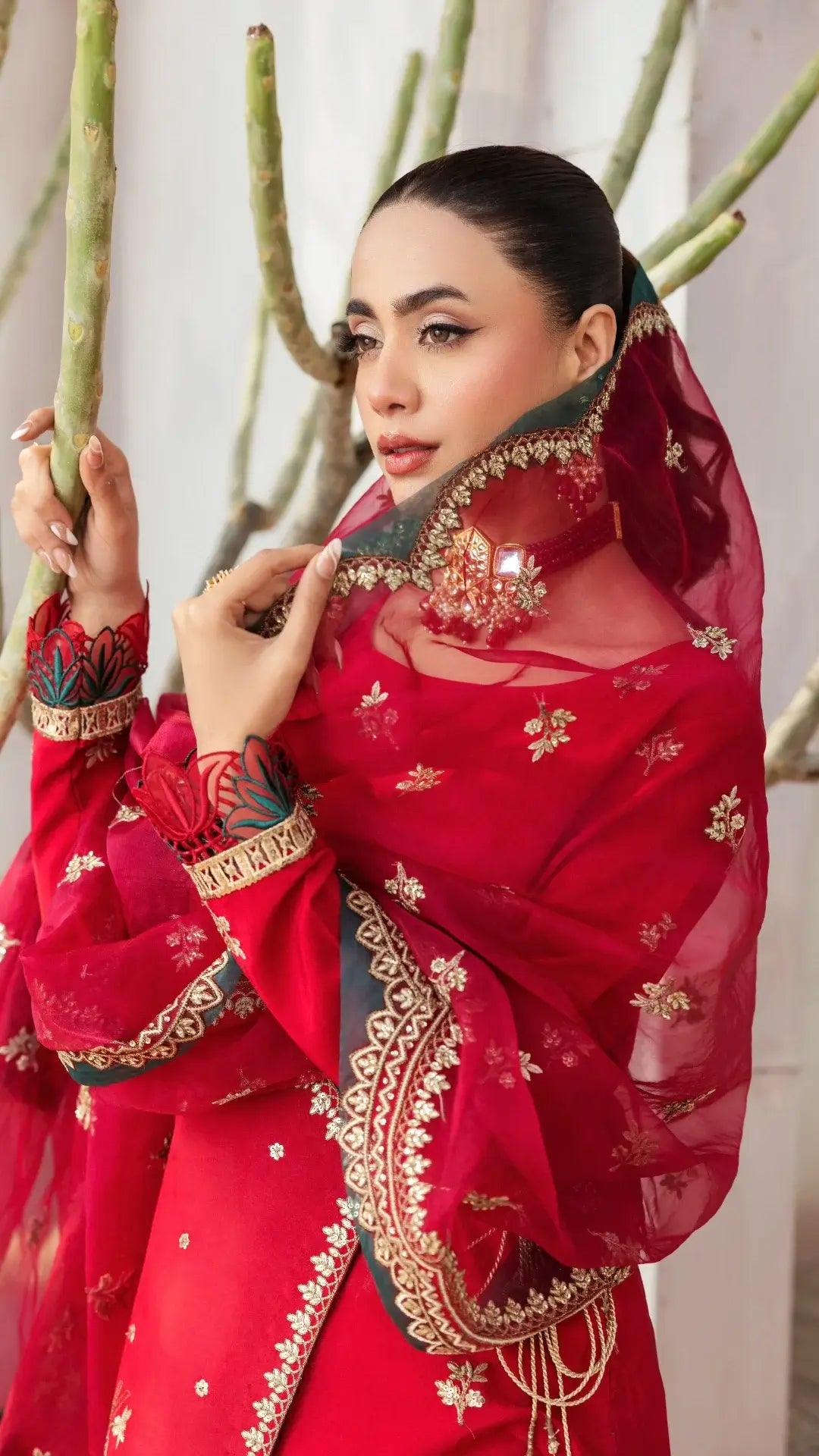 Woman wearing a red embroidered traditional outfit with gold details, standing against a neutral background.