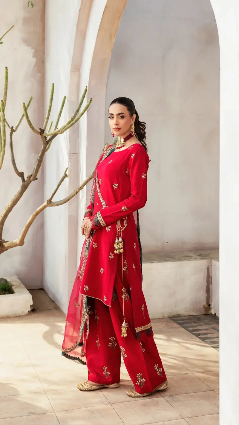 Woman in a red traditional outfit with gold embroidery standing indoors.