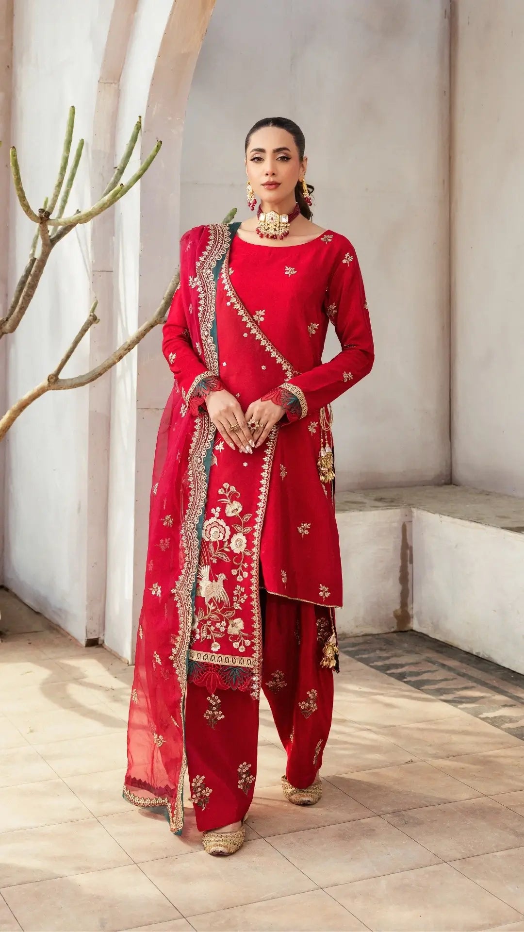 Woman in a red traditional outfit with intricate patterns standing indoors.