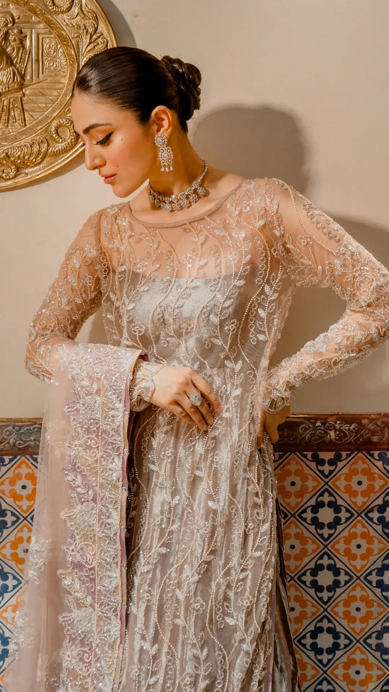 Woman in embroidered ivory formal dress with net sleeves, wearing statement jewelry, standing indoors