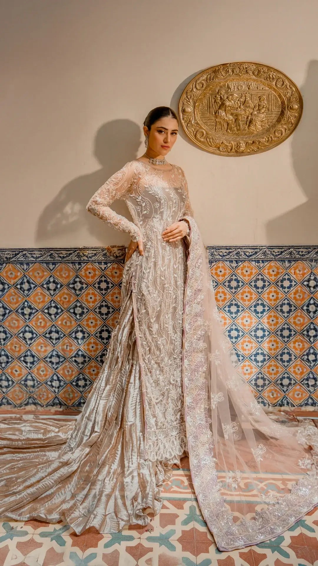 Woman in an elegant white dress standing in front of a decorative wall with tiles.