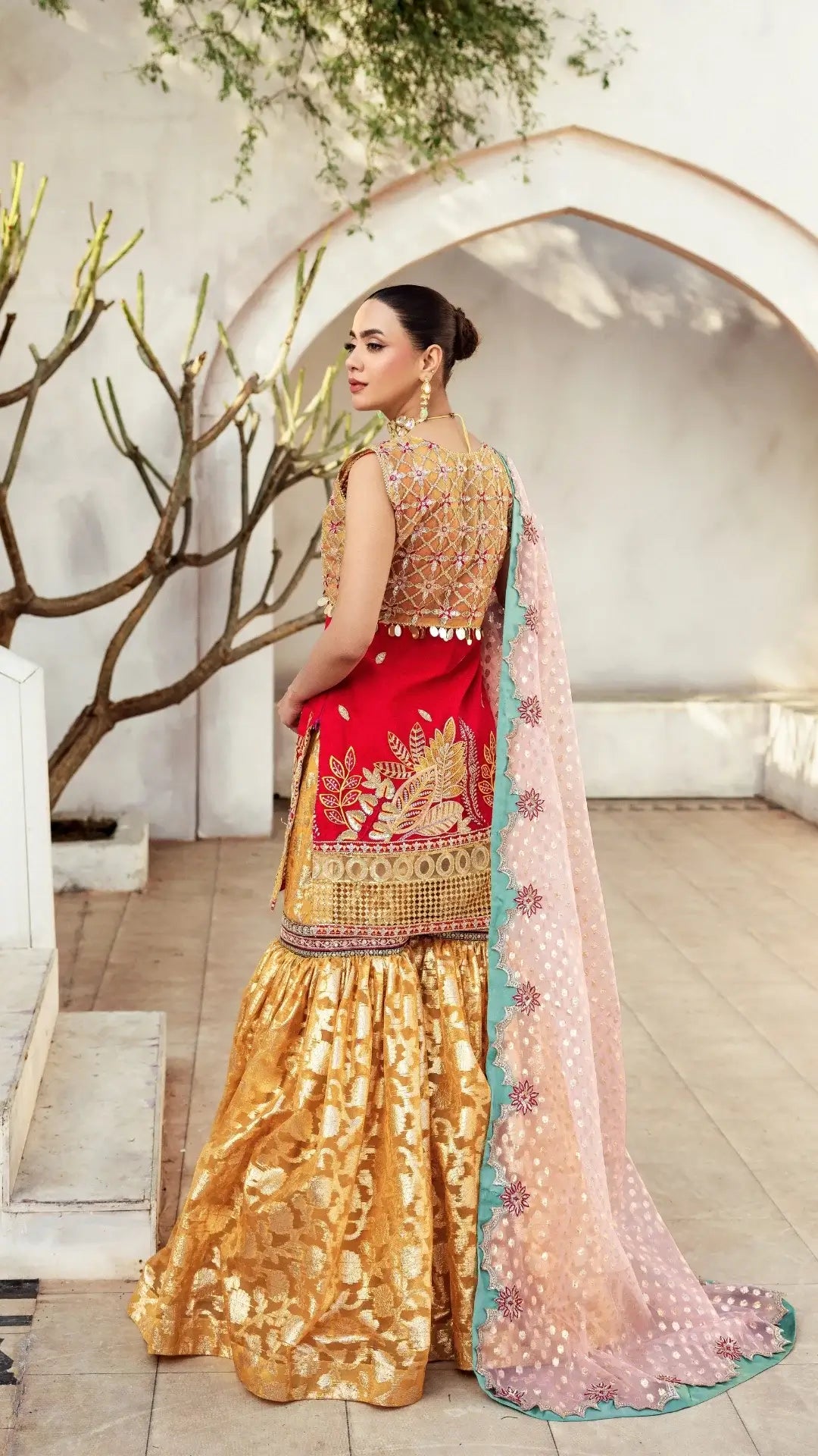 Woman in traditional Indian attire with gold, red, and pink colors in a decorated indoor setting.