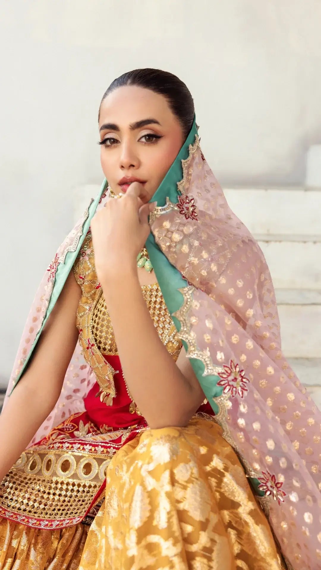 Woman wearing a traditional outfit with a pink dupatta and gold embroidery.