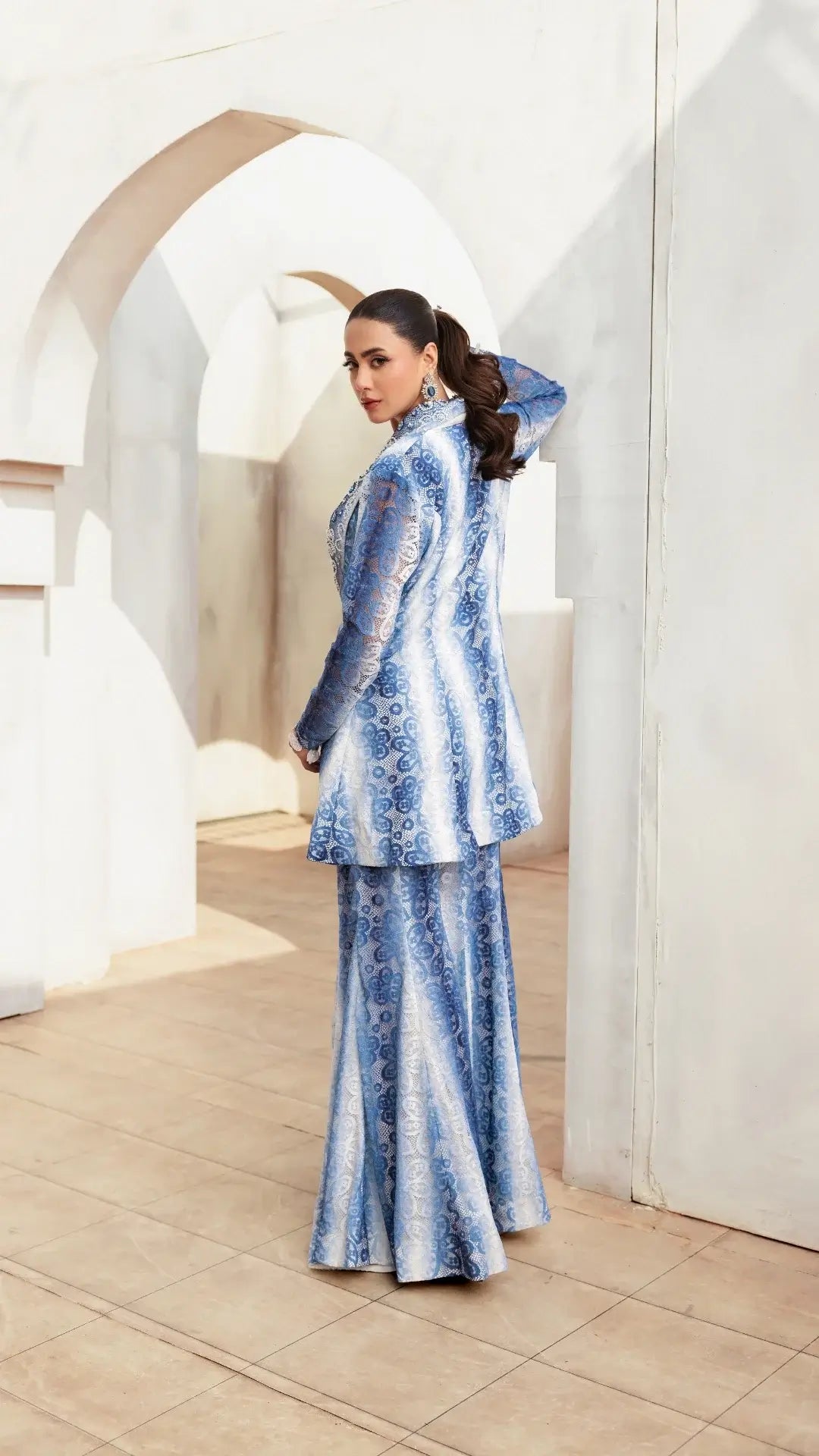 Woman in a blue and white patterned outfit standing in a modern interior setting.