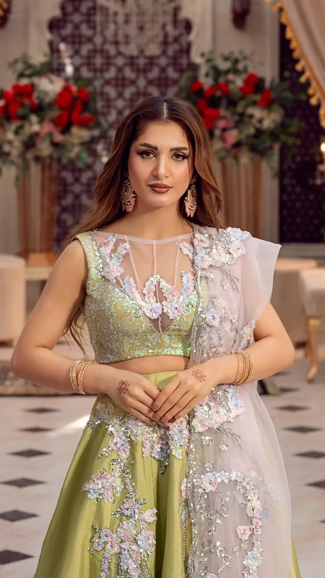 Woman in a floral embroidered outfit standing in an elegant indoor setting.