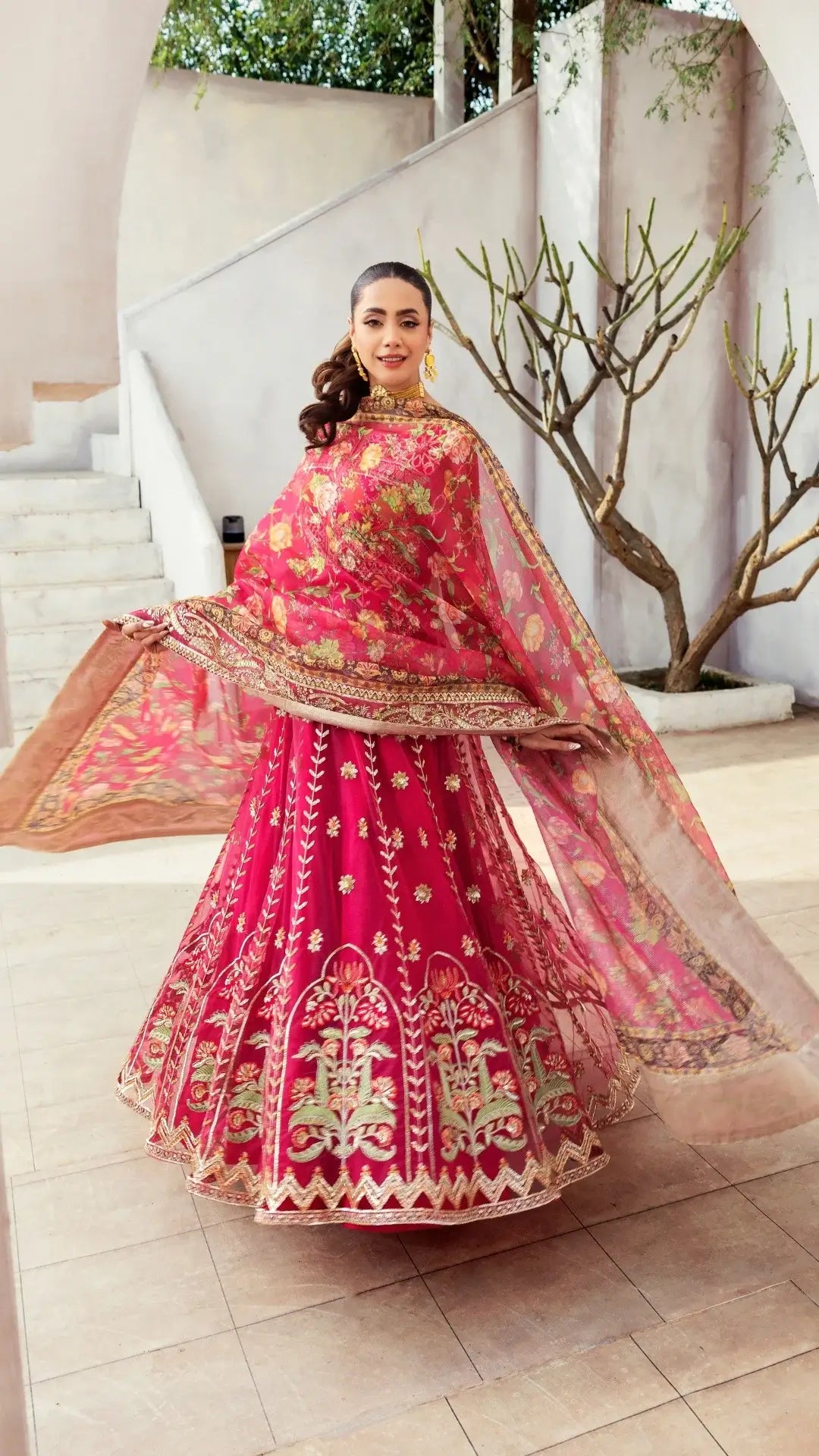 Woman in a traditional pink embroidered outfit with gold details in an indoor setting.