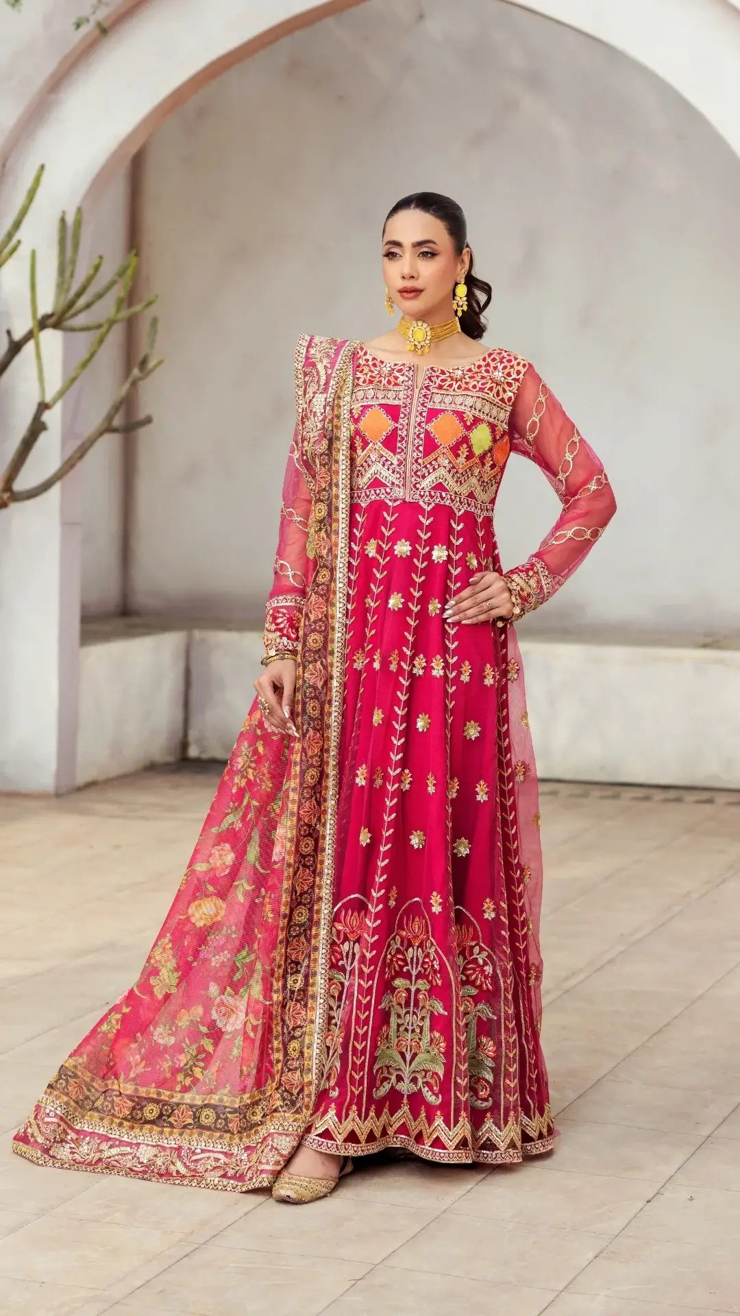Woman wearing a traditional pink embroidered outfit in an outdoor setting.