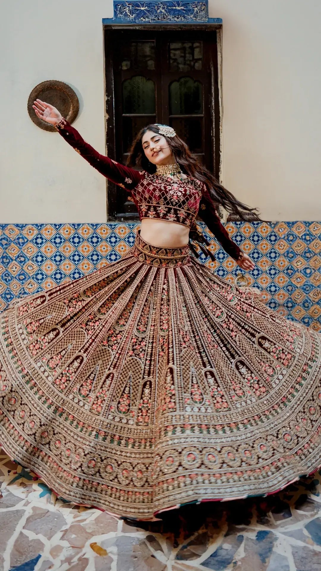 Woman in traditional embroidered outfit dancing in a room with colorful tiles.