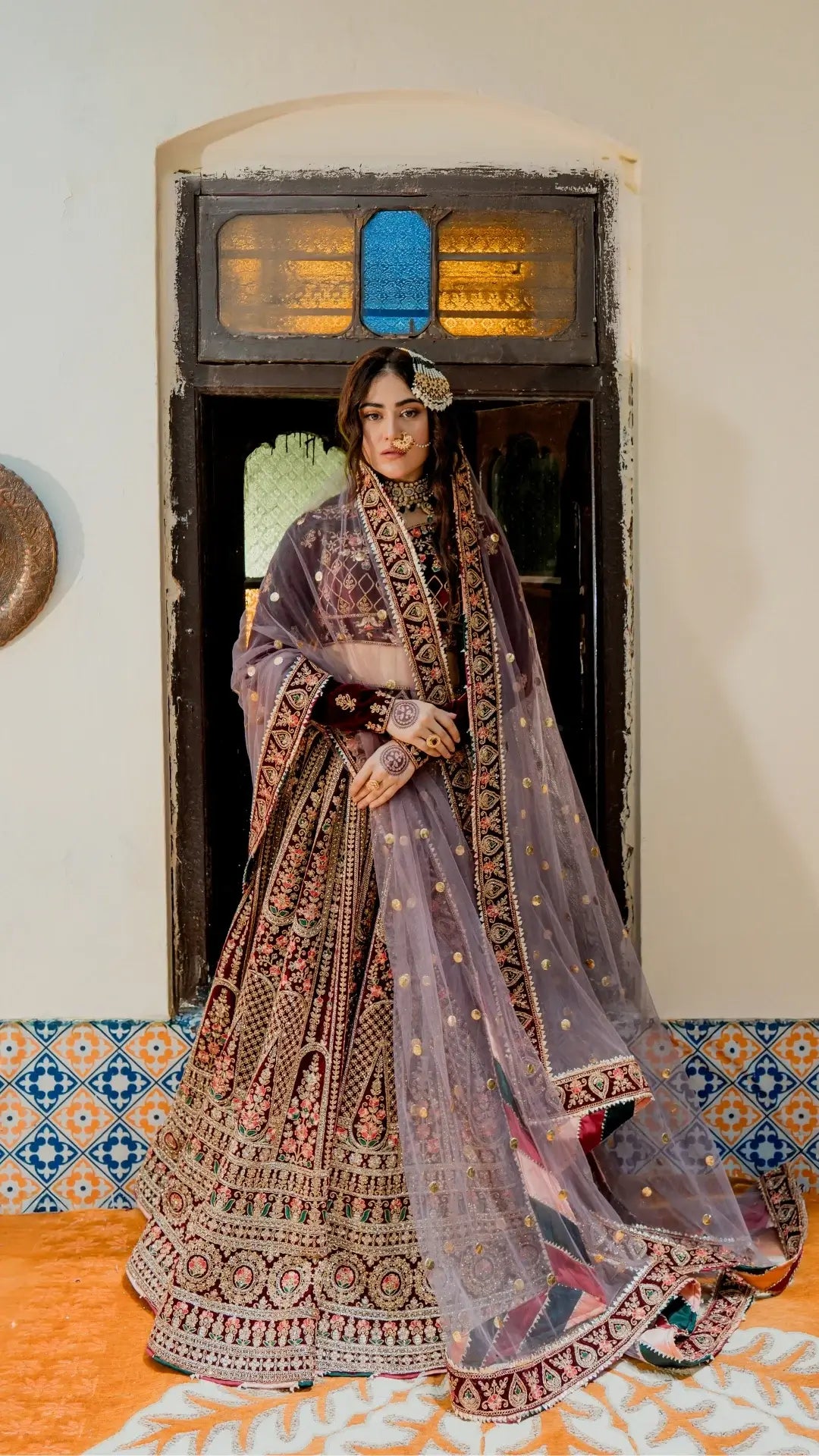 Woman in a traditional embroidered outfit with a floral headpiece, standing in a decorated room.
