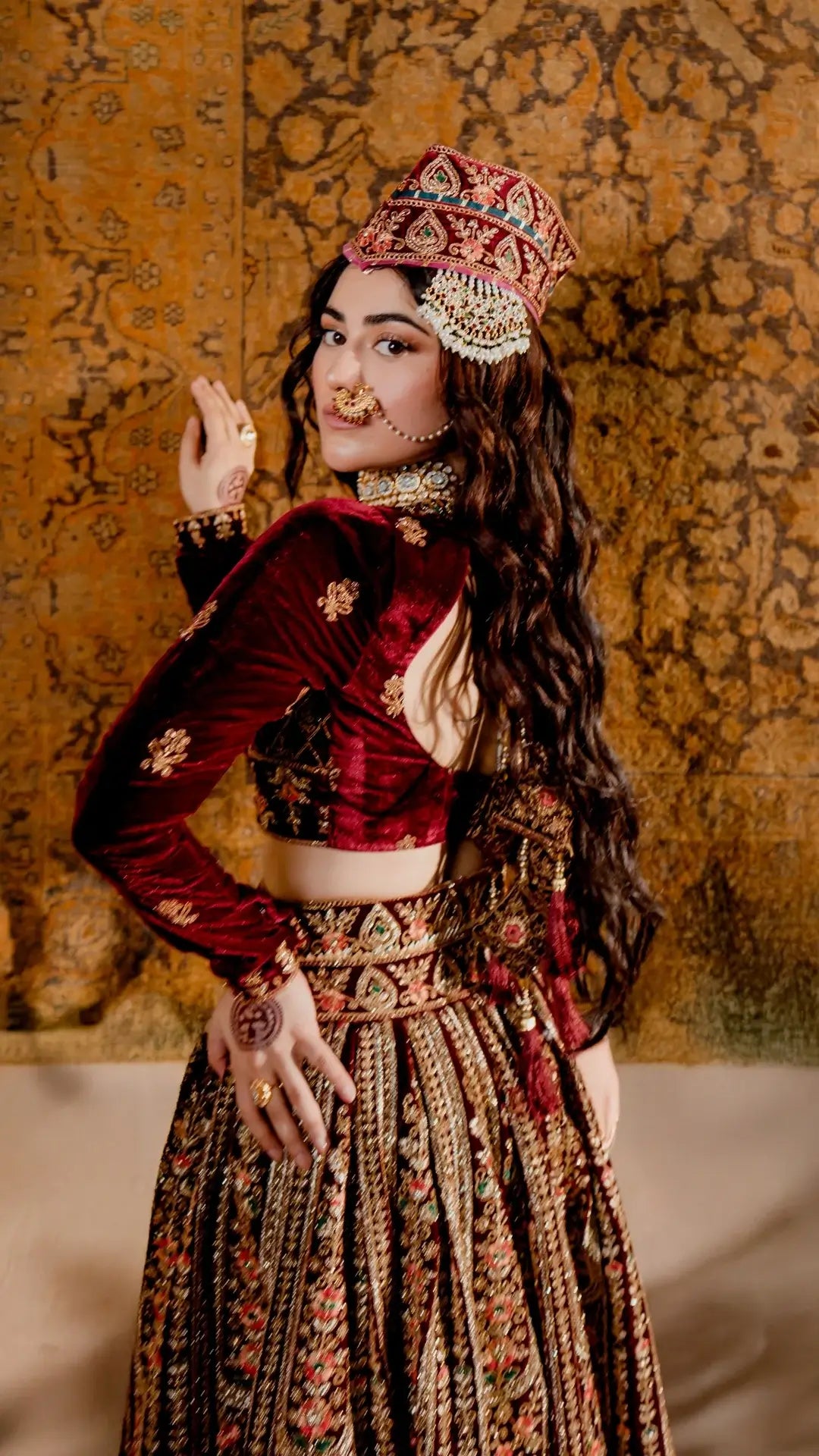 Woman in traditional attire with intricate jewelry against a textured wall.