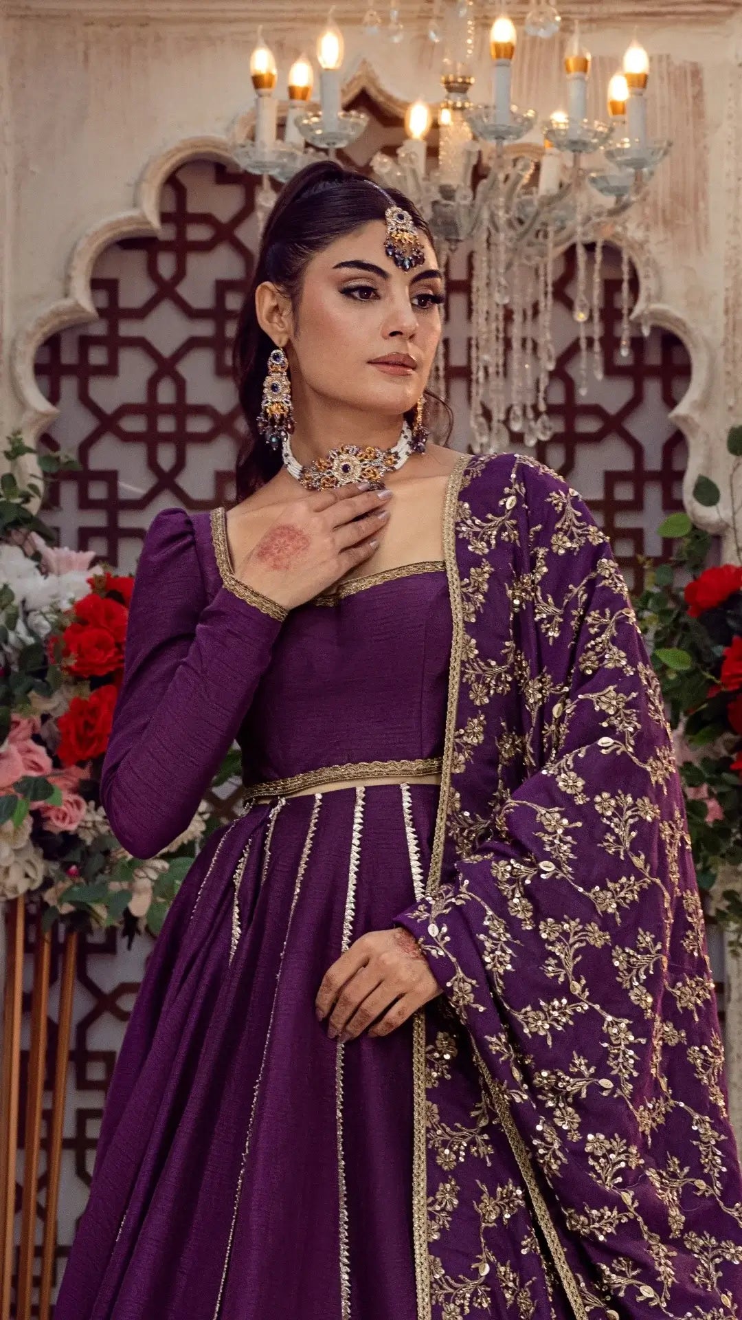 Woman in a purple traditional outfit with gold embroidery against a decorative background with flowers.