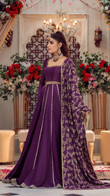 Woman in elegant purple formal Pakistani dress with gold embroidery, standing indoors
