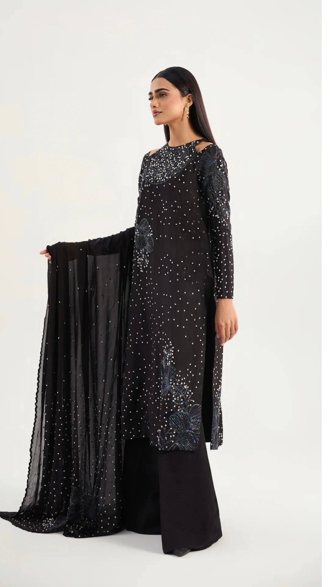 Woman wearing a black dress with silver embellishments holding a matching black scarf on a white background